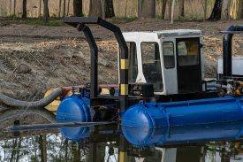 Dredge is working to remove sediment. Heavy equipment is moving silt from waterway. River restoration, flood control, and environmental engineering.